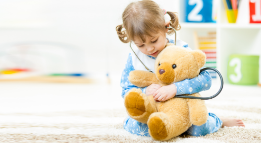 Young girl uses stethoscope on teddy bear, with toy blocks in the backgroun